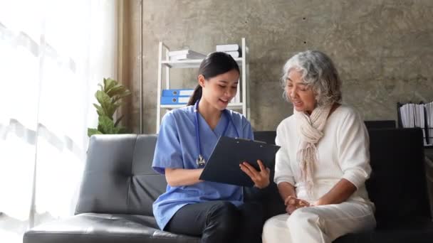 若い看護師とシニア女性は 家庭訪問中にクリップボード上の医療記録を通過します — ストック動画
