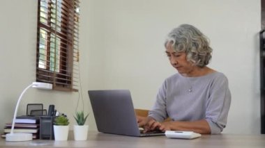 Yaşlı kadın hesaplar, yazar, faturaları internetten öder, evde çalışan mali raporları hazırlar. Odaklanmış olgun bir kadın, mali kontrol ile meşgul muhasebecilik işi yapıyor..