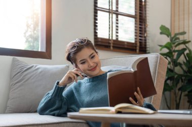 Güzel, gülümseyen bir kadın evde oturup kitap okuyor..