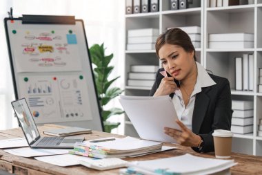 İş kadını ofis masasında dizüstü bilgisayarlı cep telefonu başında oturuyor hoş bir iş ya da gayri resmi görüşme yapıyor. Belgelerde gösterilen mali istatistiklere göre başarılı bir iş adamı.