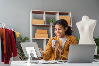 Kadın telefon ve dizüstü bilgisayar tasarımı ve ofisinden internetten bir paket gönderme. Stüdyosunda çalışan bir kadın girişimci ile teknoloji ve lojistik..