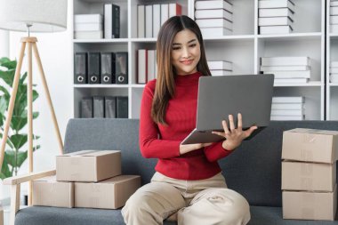 KME çevrimiçi iş fikirleri küçük işletme girişimi Asyalı bir bayan girişimci çevrimiçi siparişleri kontrol etmek ve müşteriler için paketler hazırlamak için dizüstü bilgisayar kullanır.