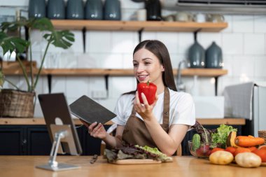 Mutfakta salatayı pişiren güzel bir bayan resmi. Tablet bilgisayarına bakılıyor.