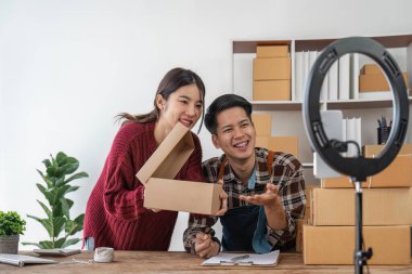 Genç çift cep telefonlarını canlı olarak çevrimiçi sosyal medyada kaydediyor ürünleri çiftler halinde satıyor, serbest çalışıyor, kendi işlerinde veya girişimcilerinde çalışıyor. E-ticaret, alışveriş konsepti.