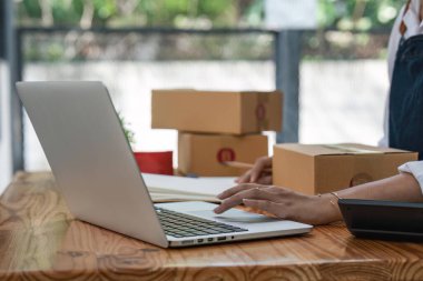 Küçük işletmeler kuran KOBİ sahipleri ve iki Asyalı kadın online siparişleri kontrol ediyor. Ev ofisinde çalışan kutucuklarla çalışan ürünler satıyorlar. Çevrimiçi küçük işletmeler kuruyorlar..