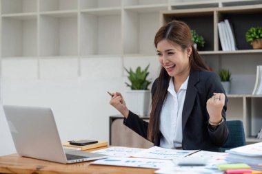 Ofisteki Asyalı iş kadını dizüstü bilgisayar kullanırken mutlu ve neşeli..