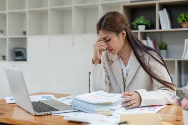 İş kadınları dizüstü bilgisayar ve belge yığınları üzerinde çalışırken stresli, iş yerinde başı ağrıyan yorgun iş kadını, işte hasta hissediyor.