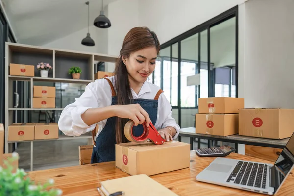 开办小企业亚洲女企业家用胶带贴包裹箱 准备根据收到的网上定单通过货运公司交货 — 图库照片