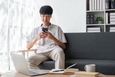 Evdeki kanepede cep telefonu kullanan yakışıklı, neşeli, mutlu ve pozitif bir adamın büyücüsü..