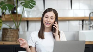 Gülümseyen genç iş kadını evde dizüstü bilgisayar kullanarak konuşuyor, mutlu bayan müşteri internet sitesinden alışveriş siparişi konseptini doğrulamak için cep telefonu görüşmesi yapıyor.