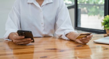 Evde kredi kartı ve akıllı telefon tutan genç Asyalı kadın tüketici çevrimiçi banka işlemleri yapıyor. Sanal alışveriş, güvenli mobil bankacılık kavramı.