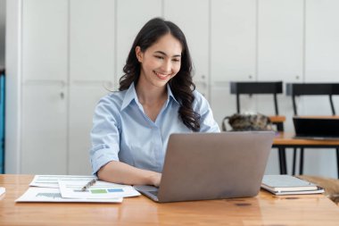 Finansal grafikler için çalışan Asyalı iş kadını yatırımları hakkında sonuçlar gösteriyor, dizüstü bilgisayarla başarılı bir iş büyüme süreci planlıyor.