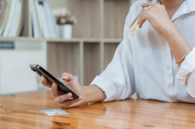 Evde kredi kartı ve akıllı telefon tutan genç Asyalı kadın tüketici çevrimiçi banka işlemleri yapıyor. Sanal alışveriş, güvenli mobil bankacılık kavramı.