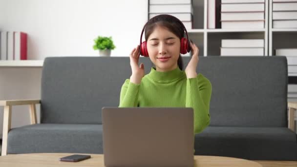 집안에 앉아서 이어폰으로 음악을 들으면서 노트북 컴퓨터를 사용하는 여성의 — 비디오