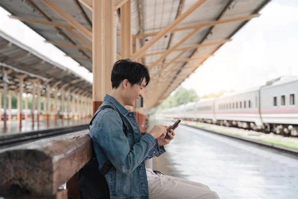 Genç Yakışıklı Adam Tren Istasyonunda Oturuyor Akıllı Telefon Kullanıyor — Stok fotoğraf