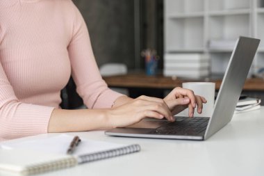 Masada oturan ve bilgisayar başında çalışan bir kadın. Kapat..