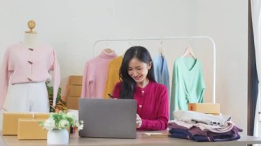 Evde internetten sipariş alan genç ve mutlu bir iş kadını. Gülümseyen moda perakende mağazası sahibi internet sitesi işletme konseptinde müşterilerle iletişim kurar.