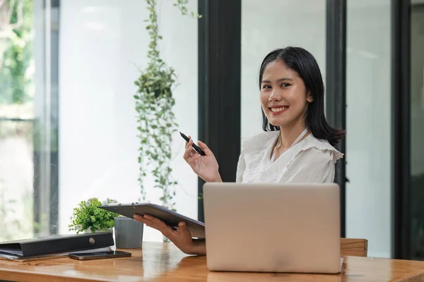 Cheerful business lady working on laptop in office, Asian happy beautiful businesswoman work in workplace. Attractive female employee office worker smile.