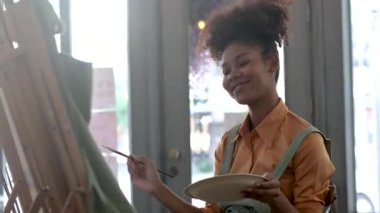 Genç Afrikalı Amerikalı stil sahibi kadın güzel sanatçı tuval üzerine izlenimcilik resmi çiziyor ve sanat stüdyosunda sanat eserleri yaratıyor..