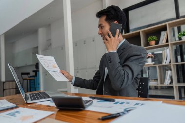 Cep telefonuyla konuşan pozitif iş adamı, modern ofiste dizüstü bilgisayarla iş yerinde oturuyor..