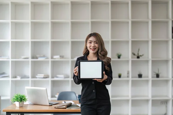 オフィスに白いデスクトップ画面があるデジタルタブレットを持っているビジネス女性のイメージ — ストック写真
