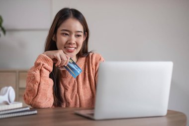 Asyalı genç bir kadının internetten sipariş verişi, evden alışveriş. Kız satın almak için internet üzerinden kredi kartı bilgilerini giriyor, alışveriş için dizüstü bilgisayar kullanıyor, bilgisayarla faturaları ödüyor.
