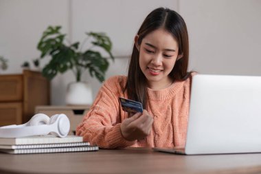 Asyalı genç bir kadının internetten sipariş verişi, evden alışveriş. Kız satın almak için internet üzerinden kredi kartı bilgilerini giriyor, alışveriş için dizüstü bilgisayar kullanıyor, bilgisayarla faturaları ödüyor.