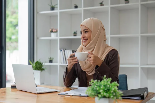 オフィスに座って窓の外を見てコーヒーマグカップを持っているアジアのイスラム教徒のビジネス女性 ビジネス関係者多様性オフィスのコンセプト — ストック写真