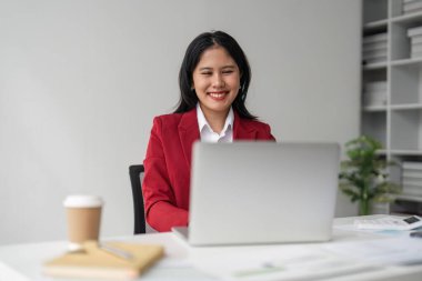 İşte oturan ve dizüstü bilgisayarda yazan güzel gülümseyen genç iş kadınının portresi..