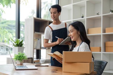 Asyalı çift aşığı siparişleri kontrol ediyor ve evdeki müşteriler için paket hazırlıyor, online satıcı kavramı.