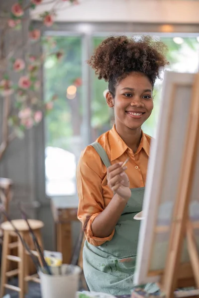 アートが好きなアフリカ系アメリカ人女性や女性アーティストが スタジオ ワークショップで紙に絵具を描きながら絵筆やパレットを持っています — ストック写真