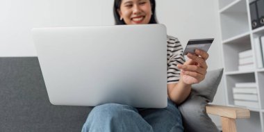 Çevrimiçi internet bankacılığı, ödeme harcamaları için kredi kartı tutan Asyalı genç kadının gülümsemesi, evde nakit olmadan para transferi veya ödemesi için dizüstü bilgisayar kullanması. Finansal Teknoloji.