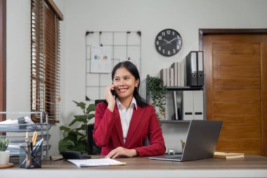 Güzel, genç, gülümseyen bir kadın, masasında oturup iş arkadaşlarıyla konuşurken ofisten uzaktan arama yapıyor..