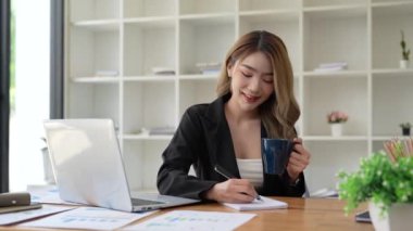 Ofisteki iş kadını dizüstü bilgisayarını kullanarak deftere sabah kahvesi ile ilgili notlar alıyor. İnsanlar ve teknoloji kavramı.