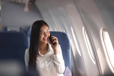 Genç uçak yolcusu iş kadını akıllı telefon iletişimi kullanıyor, iş kadını uçakta uçarken çalışıyor..