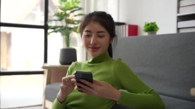 Gülümseyen mutlu Asyalı kadın internetteki e-ticaret uygulamasında alışveriş yapmayı seçen neşeli bir telefon ekranına dokunuyor.