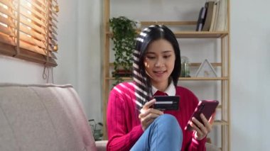 Banka kartı tutan mutlu kadın, cep telefonu internet alışveriş uygulamasına CVV kodu ya da ödeme bilgisi giriyor.