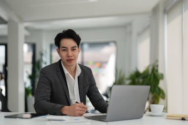 Genç Asyalı iş adamı yönetici şirket ofisinde dizüstü bilgisayarla finans stratejisi üzerinde çalışıyor. Profesyonel iş adamı masada bilgisayar teknolojisi kullanıyor..