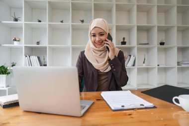 Müslüman güzel iş kadını ofiste cep telefonuyla konuşuyor..