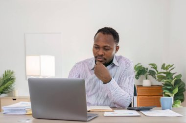 İş adamı siyahi adam evde dizüstü bilgisayar kullanıyor. Olgun iş adamı mutlu bir şekilde e-posta yollar ve evde çalışır. Kağıt işleri ve belgeler ile bilgisayarda yazan Afrikalı Amerikalı bir adam..