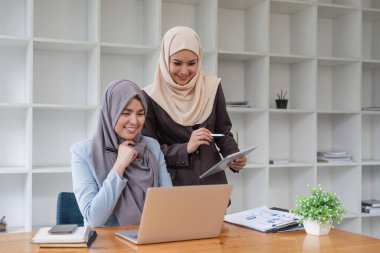 Genç Müslüman kadın iş adamı arkadaşlarıyla oturup, bilgisayarla ve finansal belgelerle masaya oturarak tartışıyor..