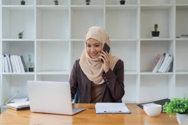 Müslüman güzel iş kadını ofiste cep telefonuyla konuşuyor..