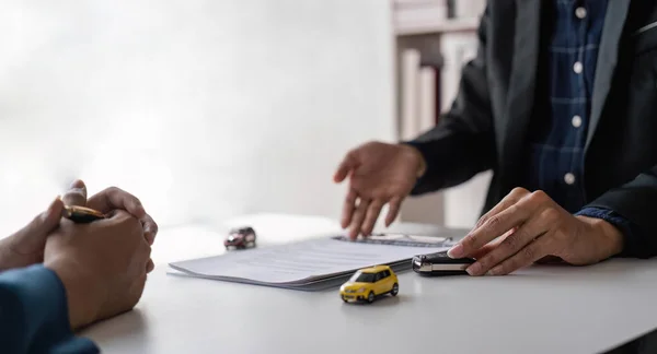 signing car insurance document or lease paper. Writing signature on contract or agreement. Buying or selling new or used vehicle. Car keys on table. Warranty or guarantee. Customer or salesman.