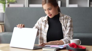 Neşeli Asyalı kadın dizüstü bilgisayarını açıp daktilo ediyor. Genç bayan profesyonel evinden önemli bir e-posta yazıyor. Modern oturma odası. Uzak çalışma.