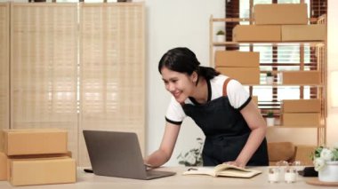 Başlangıçta küçük işletme KOBİ 'si, dizüstü bilgisayar kullanan girişimci kadın paket ürün kutusu hazırlamak için çevrimiçi alışveriş siparişini alır ve kontrol eder.