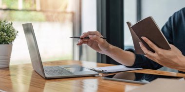 Ofiste çalışan Asyalı işadamı dizüstü bilgisayarla yeni bir iş kuruyor ve not defterine yazıyor, görüntüyü kapatıyor.