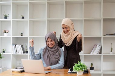 Toplantıda çalışan ve iş tartışan iki genç Müslüman kadın toplantı odasında mali grafikler ve dizüstü bilgisayarlarla iyi haberler almaktan memnuniyet duyuyorlar..