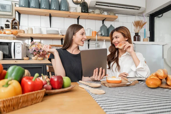 stock image Happy two young women looking tablet computer during cooking together in kitchen room at home. Two young diverse lesbian women spending time together. LGBT and gender identity concept.