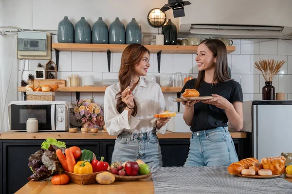 Two beautiful woman friends enjoy breakfast in kitchen drinking coffee. Two best friends LGBTQ relation partner home cooking. Two woman together love friendship.