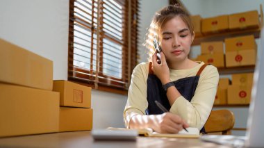 Küçük işletme girişimi KOBİ sahibi Asyalı kadın siparişleri kontrol ediyor kutularla çalışan ürünler satıyor. evde ve çevrimiçi KOBİ 'de bağımsız olarak çalış.